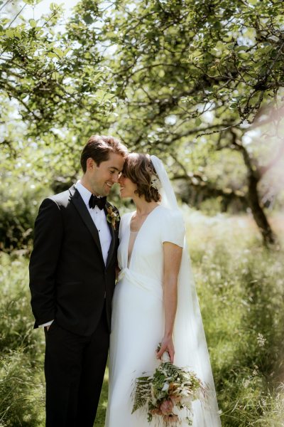 Bride and groom touch foreheads in forest setting