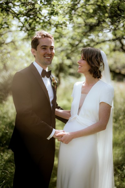 Bride looks at groom as her poses for the camera laughing smiling