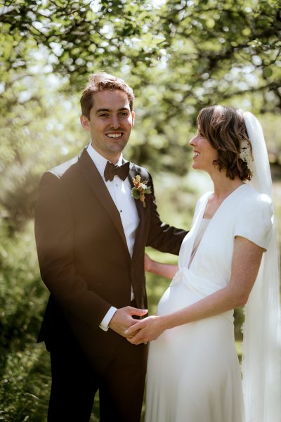 Bride looks at groom as her poses for the camera laughing smiling