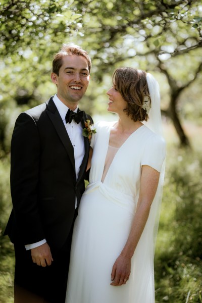 Bride looks at groom as her poses for the camera