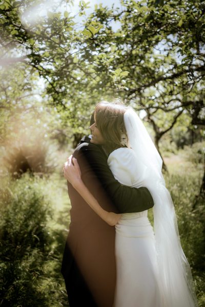 Bride and groom hug embrace on grass sun shining through trees forest setting