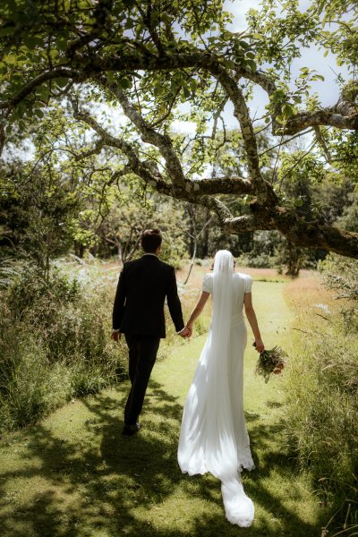 Bride and groom walk along the grass together from behind