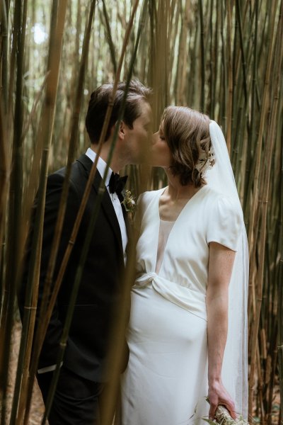 Bride and groom kiss amongst the trees in forest