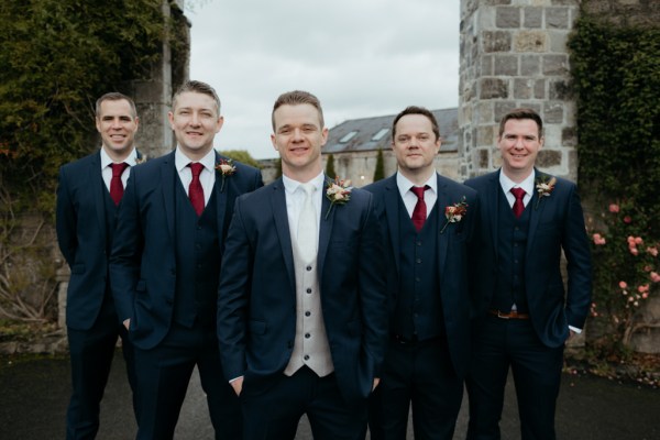 Groom and groomsmen stand beside pillars