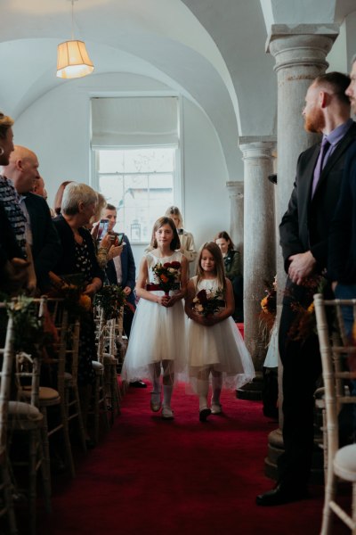 Two flower girls little girls walk down the aisle holding flowers