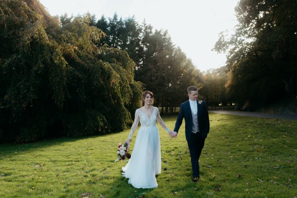 Bride and groom walk along grass park forest area