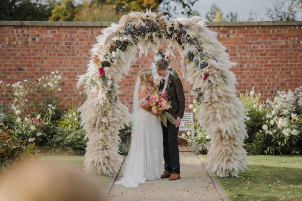 Bride and groom look at each other bouquet of flowers in shot surrounded by flowers overhead