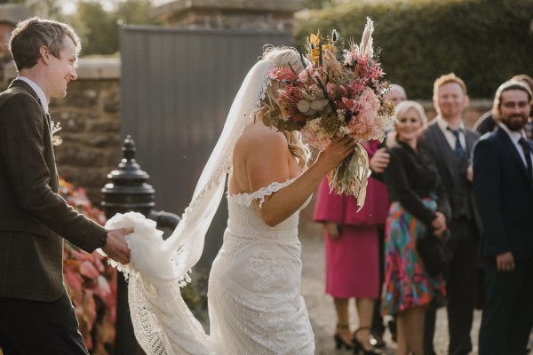 Bride walks with groom holding up dress as she walks