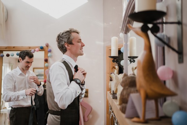 Groom looks in the mirror fixing tie