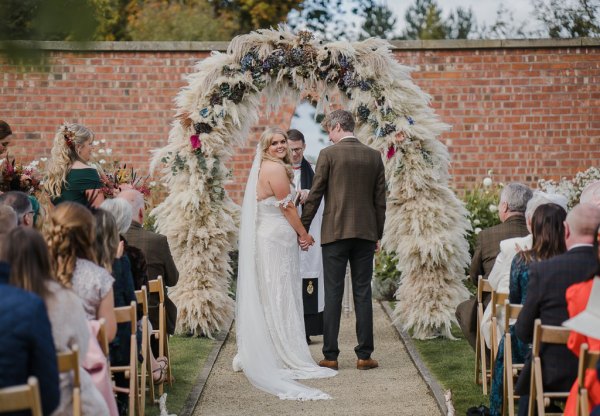 Bride and groom before priest smile looks over shoulder