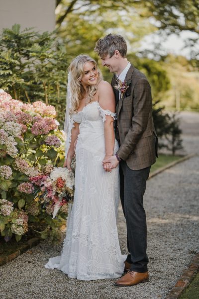 Bride and groom smiling at each other in garden forest setting bouquet of flowers