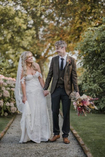 Bride and groom walk hand in hand outside wedding venue bouquet in shot