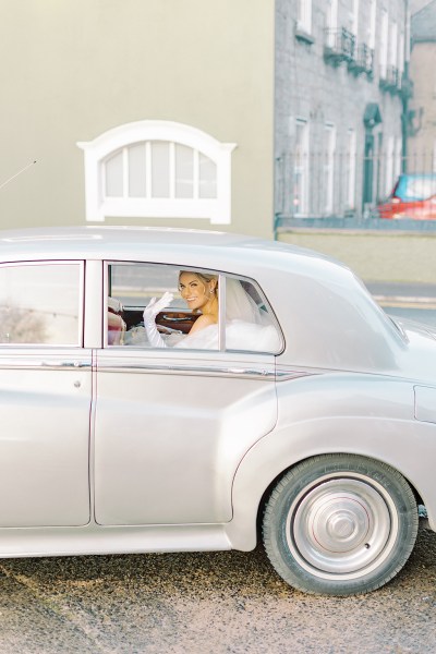 Bride waving inside wedding car