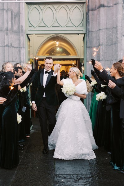 Bride and groom hand in the air exiting church with guests