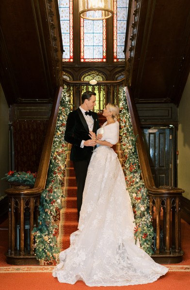 Bride and groom standing at bottom of staircase lights holly surround them