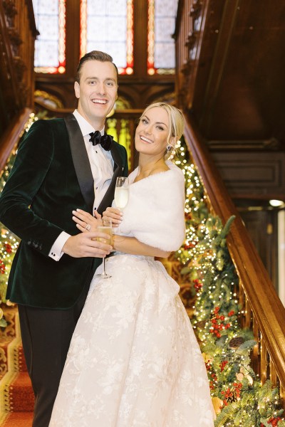 Bride and groom standing at bottom of staircase lights holly surround them smiling laughing