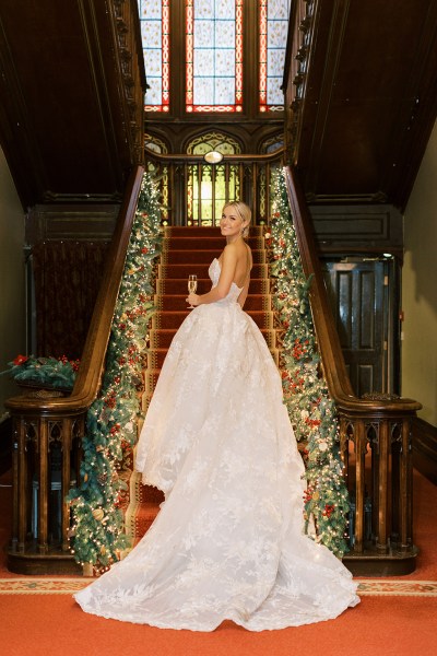 Bride stands on the red staircase carpet surrounded by lights and holly decorations