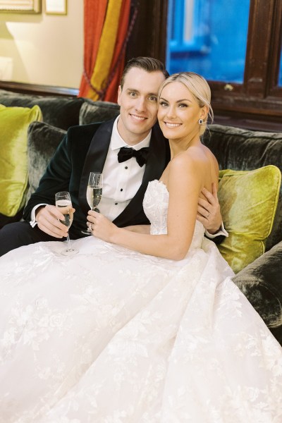 Bride and groom hold glass of prosecco sitting on couch