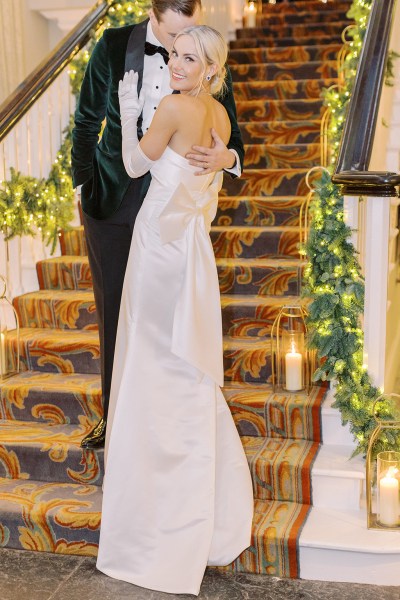 Groom places hand on back of bride bow ribbon white dress gown detail