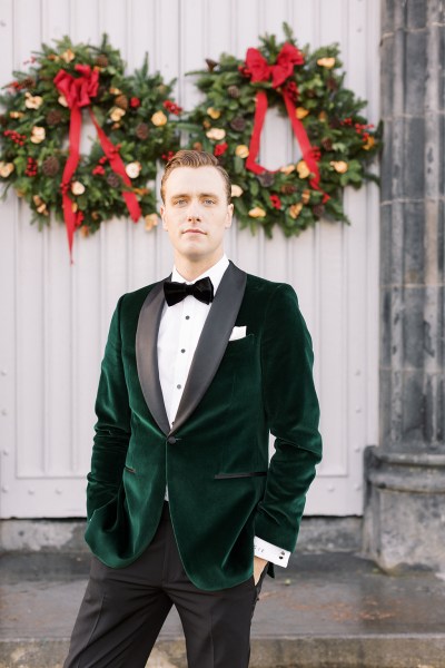 Groom stands outside exterior shot wreath hanging behind him on door