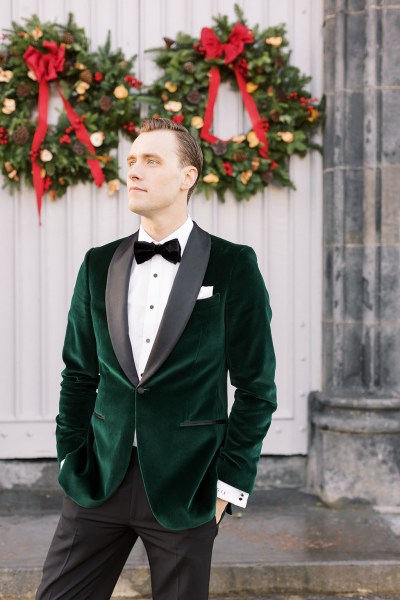 Groom stands outside exterior shot wreath hanging behind him on door