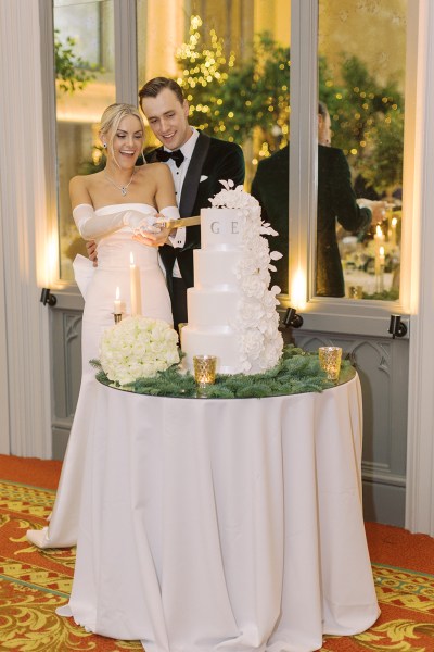 Bride from behind bow detail on dress gown and groom cutting the white wedding cake