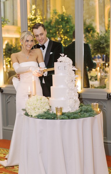 Bride from behind bow detail on dress gown and groom cutting the white wedding cake