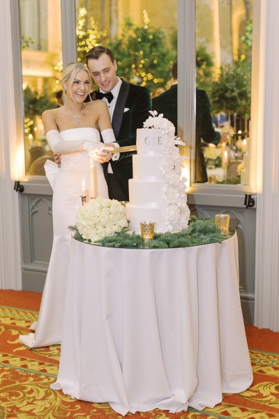 Bride from behind bow detail on dress gown and groom cutting the white wedding cake