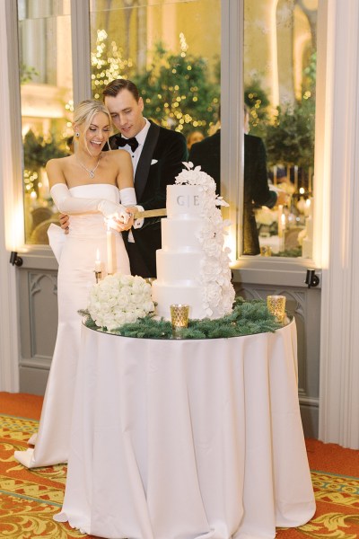 Bride from behind bow detail on dress gown and groom cutting the white wedding cake