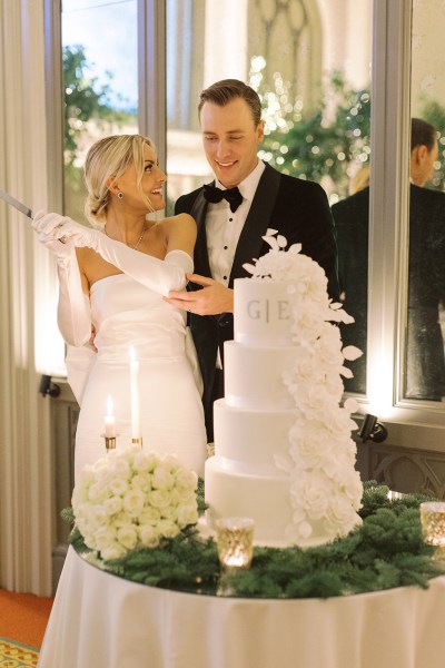 Bride from behind bow detail on dress gown and groom cutting the white wedding cake