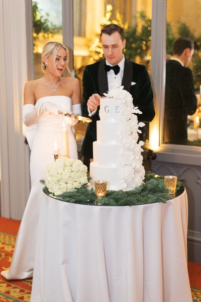 Bride from behind bow detail on dress gown and groom cutting the white wedding cake