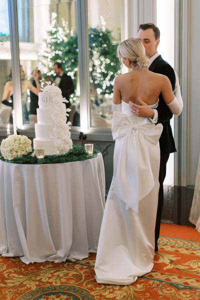 Bride from behind bow detail on dress gown and groom cutting the white wedding cake