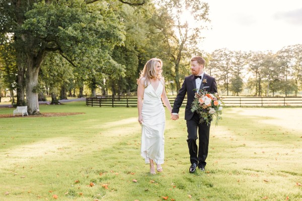 Bride and groom walk on grass hand in hand