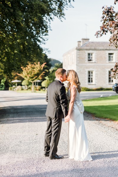 Bride and groom kiss on pathway outside wedding venue