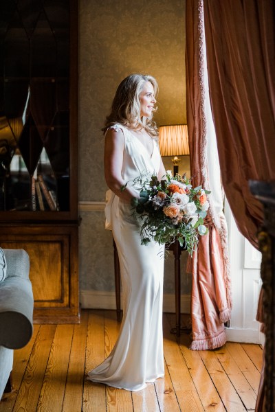 Bride stands at the window holding bouquet of flowers