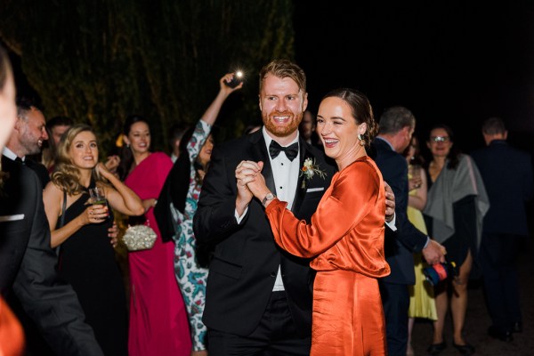 Groom dances with woman in orange silk gown