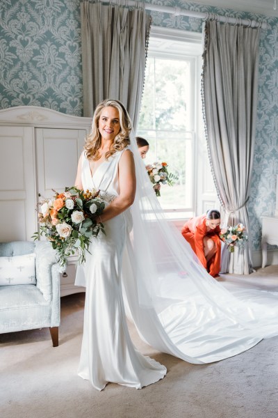 Bride poses in bright white room with bridesmaids behind her