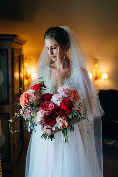 Bride holds flowers red and pink bouquet veil interior shot looking down