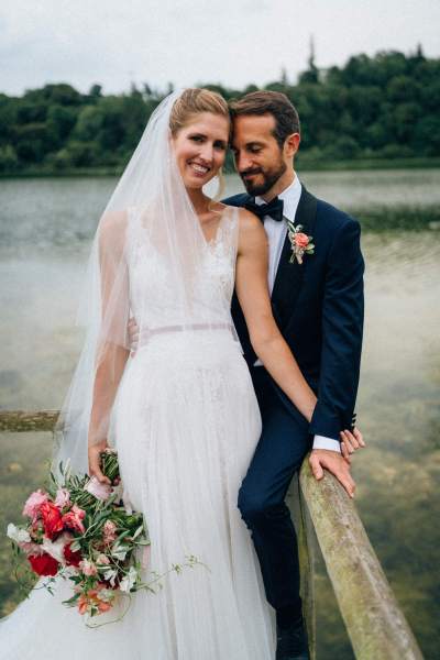 Bride and groom hug/hold each other in front of lake on boardwalk