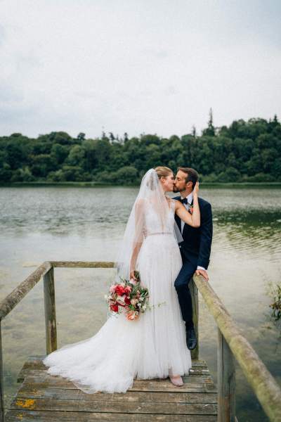 Bride and groom kiss in front of lake on boardwalk