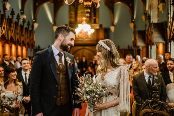 Groom smiles at bride as she holds bouquet