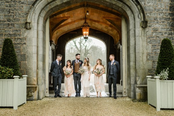 bride groom bridesmaids and groomsmen walk under archway to wedding venue