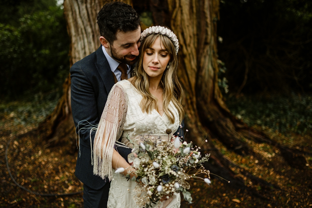 Groom hugs bride from behind as she holds bouquet