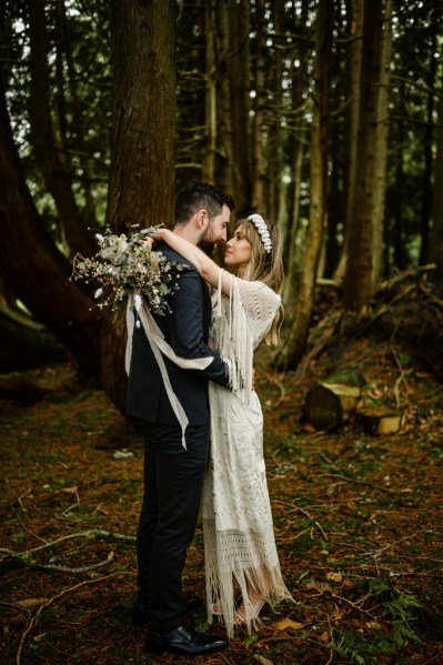 Bride wraps her arms around grooms neck in forest setting