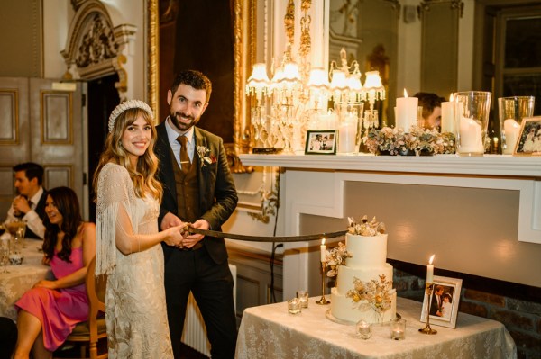 Bride and groom about to cut the white wedding cake with sword