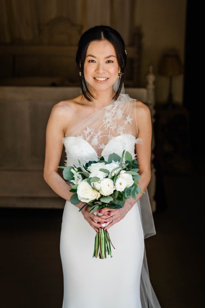 Bride poses on her own looks down at white roses flowers bouquet