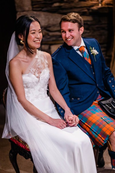 Bride and groom smile look at each other holding hands