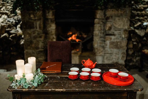 Tea is poured from red teapot beside white candles