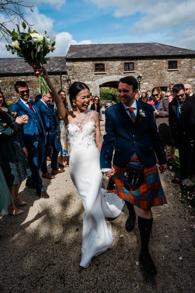 Bride and groom celebrate guests clapping bouquet in the air