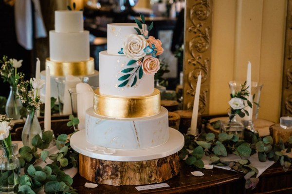 Close up of white wedding cake with roses and gold painted design